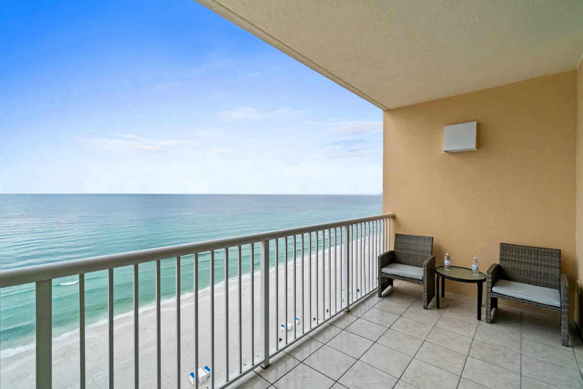 A private balcony with comfortable seating overlooks the sandy beach and endless ocean, with a clear blue sky above. The space is ideal for enjoying morning coffee or evening cocktails while listening to the soothing sound of waves, as described in the narrative.