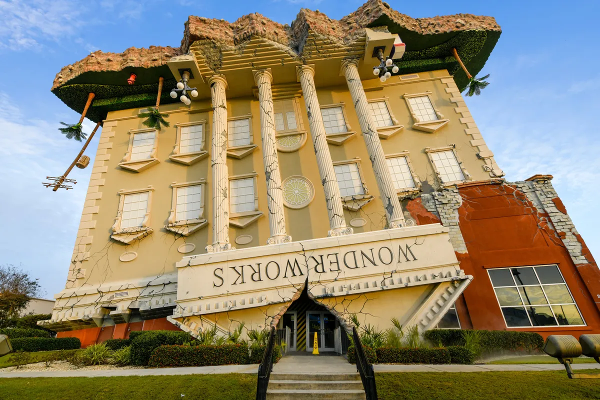 An upside-down building with dramatic architectural details and the 'WONDERWORKS' sign, surrounded by lush landscaping and a welcoming entrance pathway. Visitors are seen exploring, hinting at the interactive and educational fun inside.