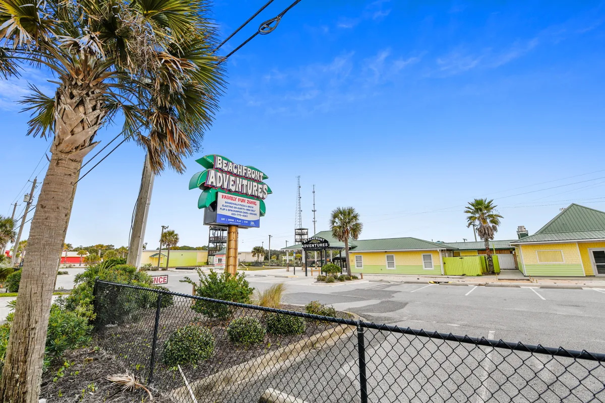 A bright, inviting entrance to Beachfront Adventures, featuring the 'Family Fun Zone' sign, palm trees, and cheerful yellow buildings. The empty parking lot and signage evoke anticipation for fun group activities and seasonal attractions.